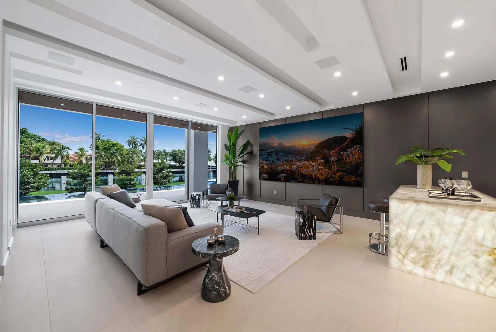 Expansive VIP lounge with floor-to-ceiling glass, serene waterfront views, custom wall paneling, oversized television, and direct access to the outdoor living area.