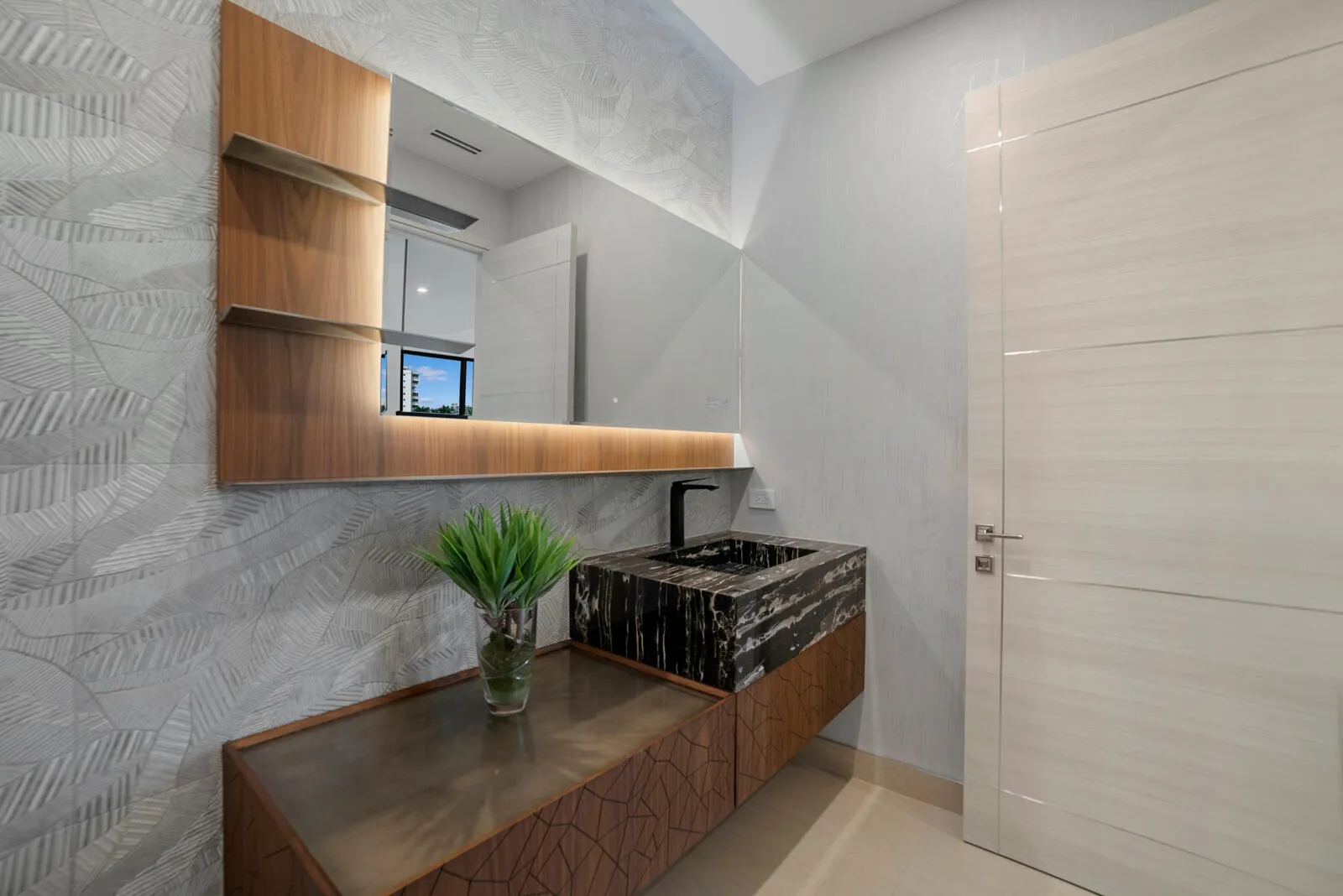 Sophisticated first-floor powder room featuring a dramatic stone vessel sink, floating custom vanity, textured designer wallcovering, and an illuminated oversized mirror.