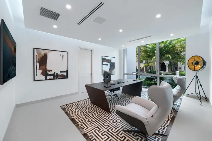 Sophisticated first-floor executive office featuring floor-to-ceiling windows, contemporary designer finishes, abundant natural light, and serene views of the tropical landscaping.