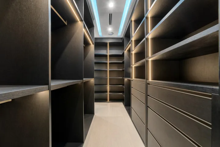 Custom gentleman’s walk-in wardrobe featuring dark wood cabinetry, extensive shelving and hanging space, integrated drawers, and sophisticated lighting.