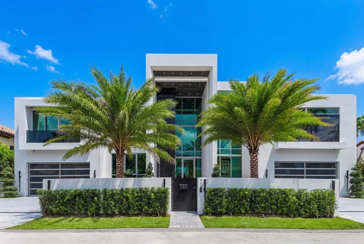 Striking modern architecture with dramatic floor-to-ceiling glass, dual garages, lush tropical landscaping, and an impressive grand entrance.
