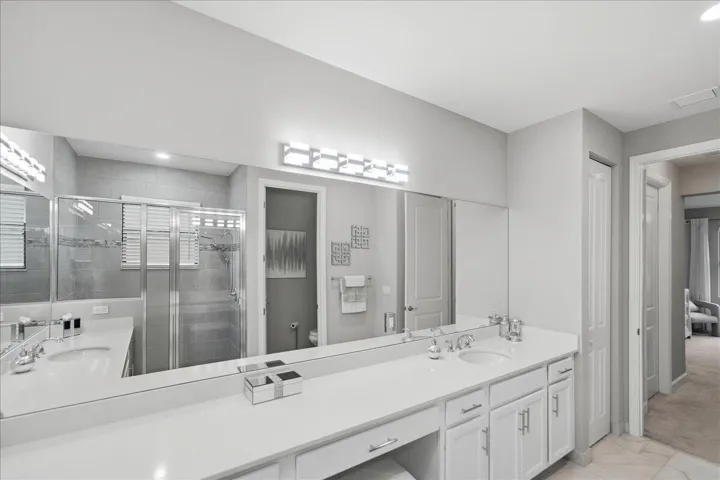 Dual sink vanity with white cabinetry, integrated makeup area, and full-width mirror