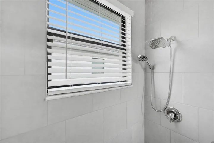 Shower with light grey tile surround, dual shower heads, and chrome fixtures
