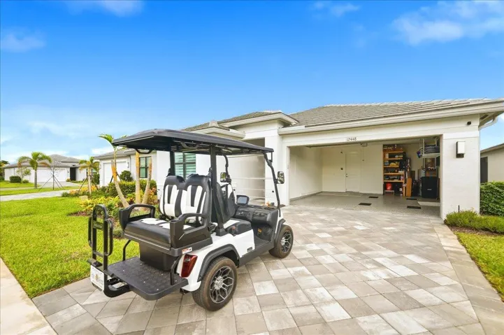 Paver driveway with a single-car garage and an open bay, featuring a low-pitched tile roof and manicured landscaping