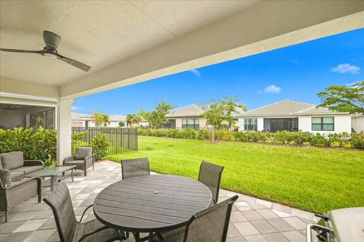 Covered patio featuring a ceiling fan, patterned paver flooring, and a expansive grassy area