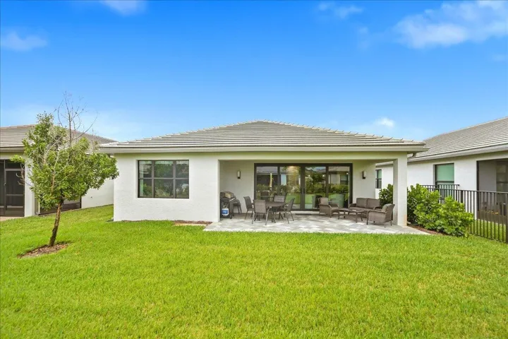Expansive green lawn, covered patio with paver flooring, sliding glass doors, multiple windows, and a tiled roof