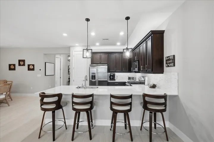 Spacious kitchen featuring dark wood cabinetry, white countertops, stainless steel appliances, and two pendant light fixtures