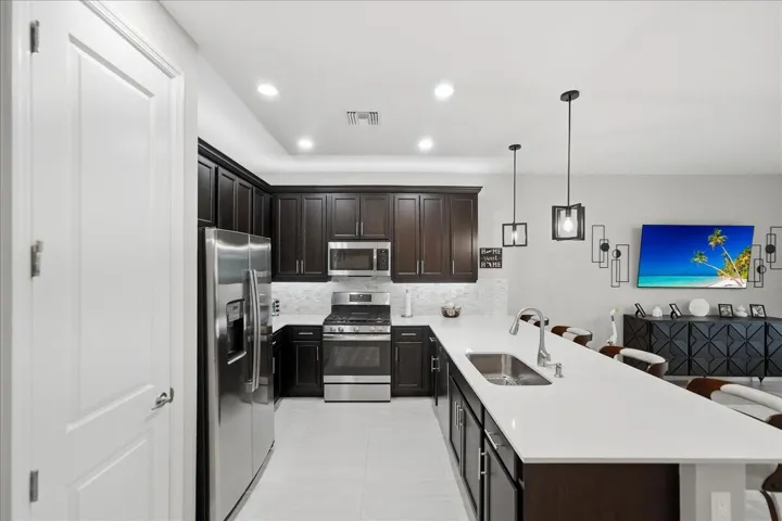 Kitchen featuring dark wood-finish cabinetry, stainless steel appliances, white countertops, and a subway tile backsplash