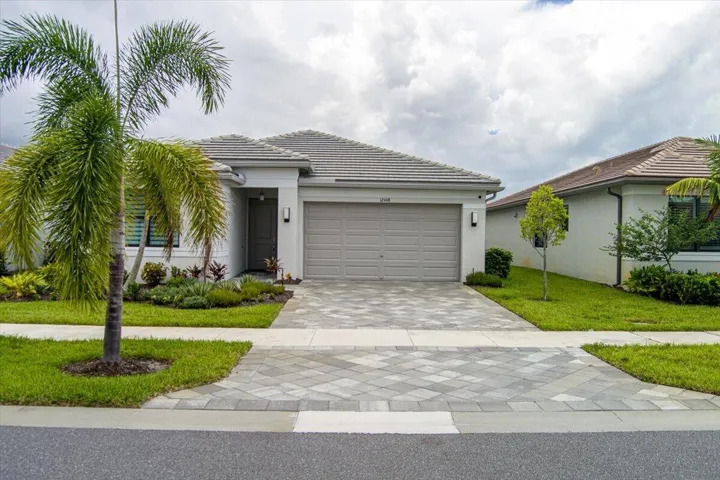 Paver driveway, front-facing garage, manicured landscaping, palm trees, and modern exterior lighting