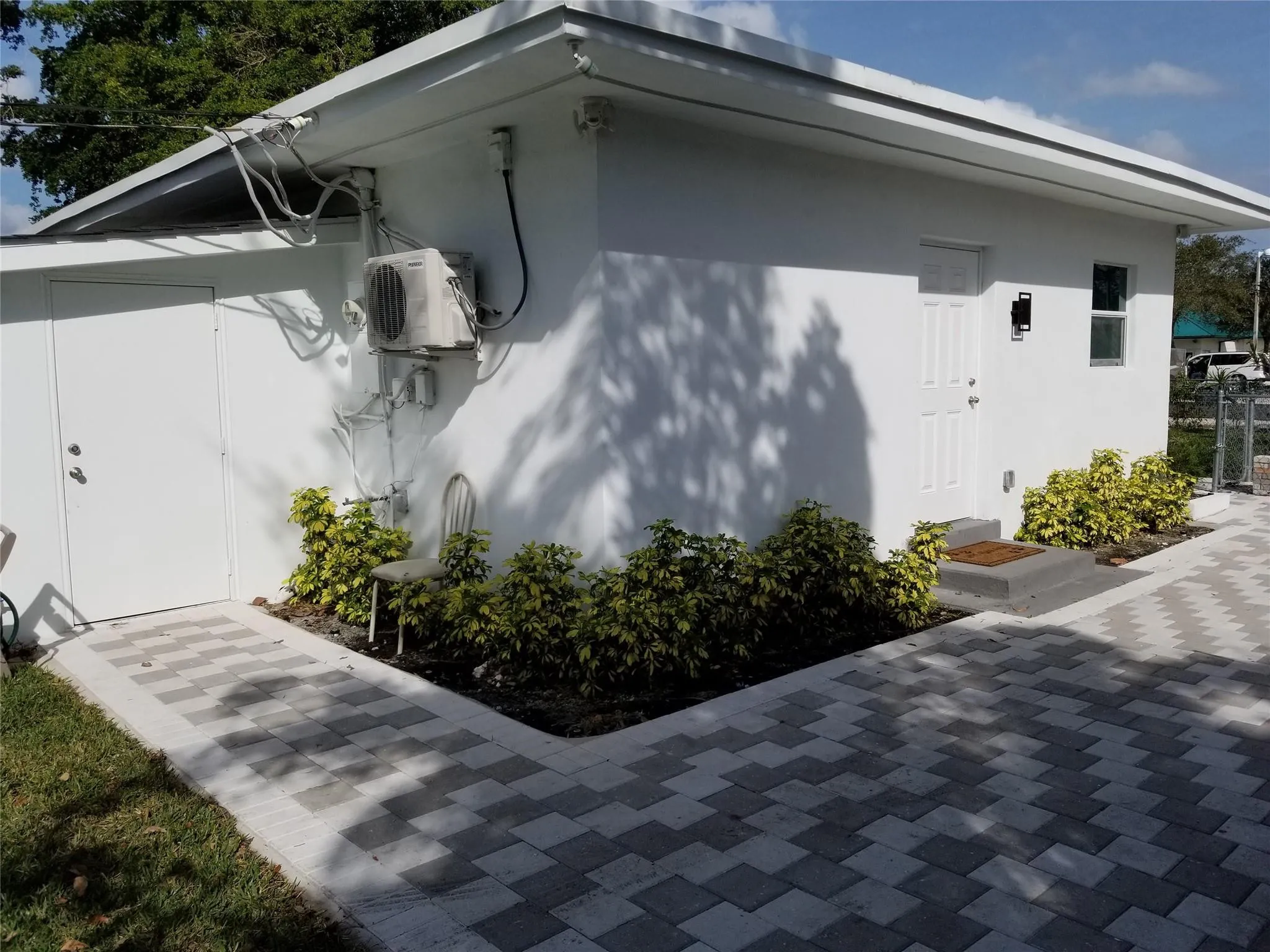 White stucco exterior, two-tone paver pathways, mature landscaping, and an external entry door