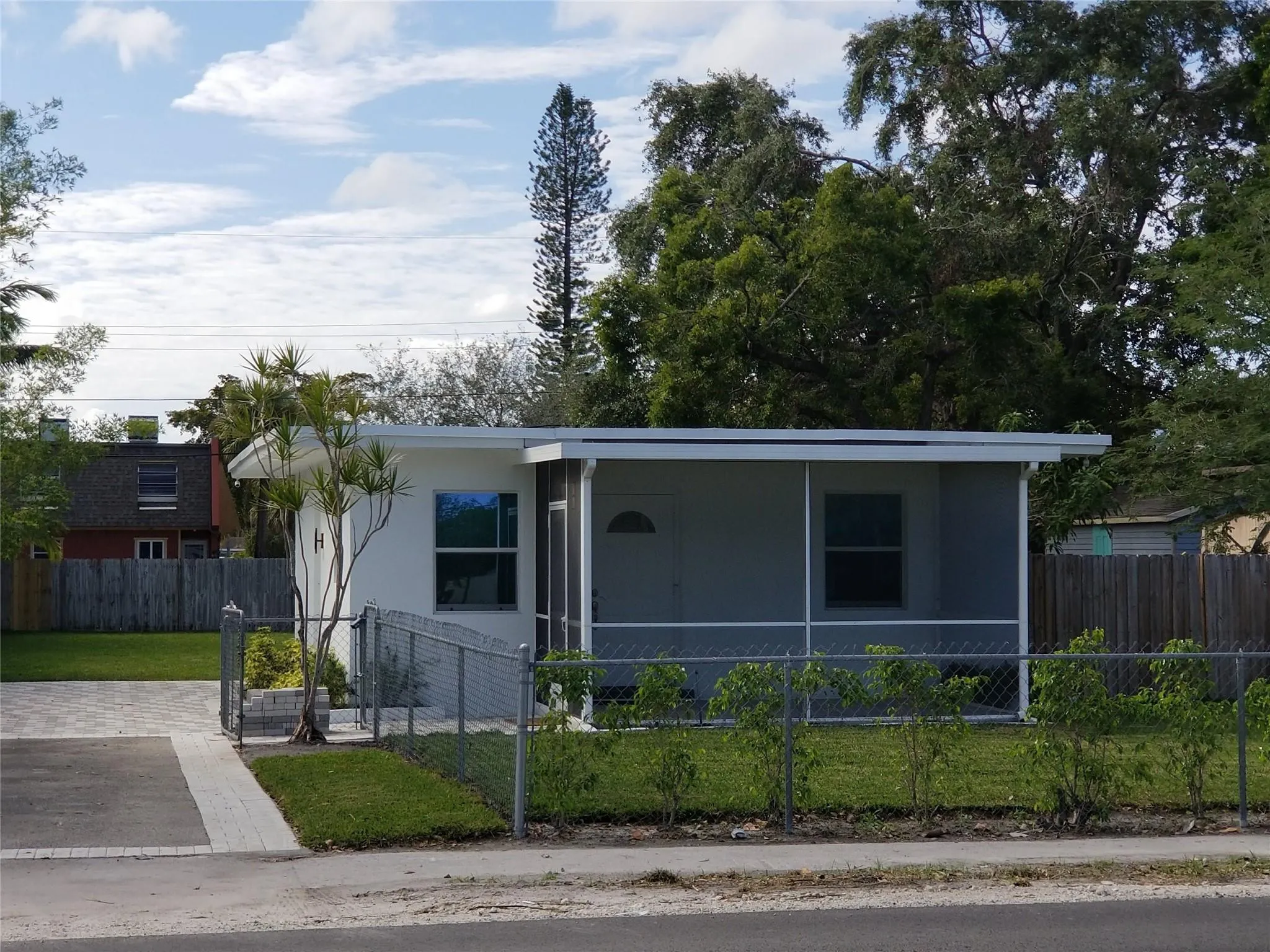 White exterior with screened porch, chain-link fencing, and paved driveway