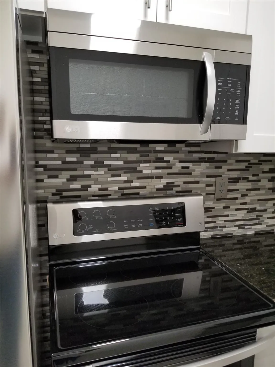 Stainless steel microwave, electric range with a smooth cooktop, mosaic tile backsplash, and dark countertop