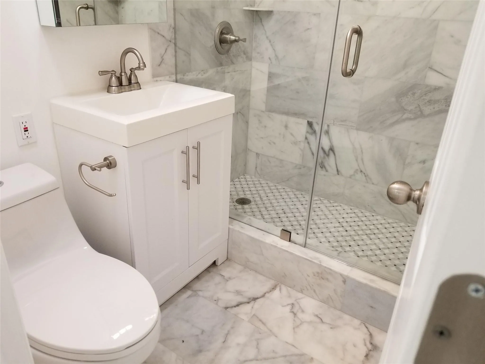 White vanity with brushed nickel hardware, walk-in shower with glass enclosure, white square vessel sink, and marble-finish tile flooring