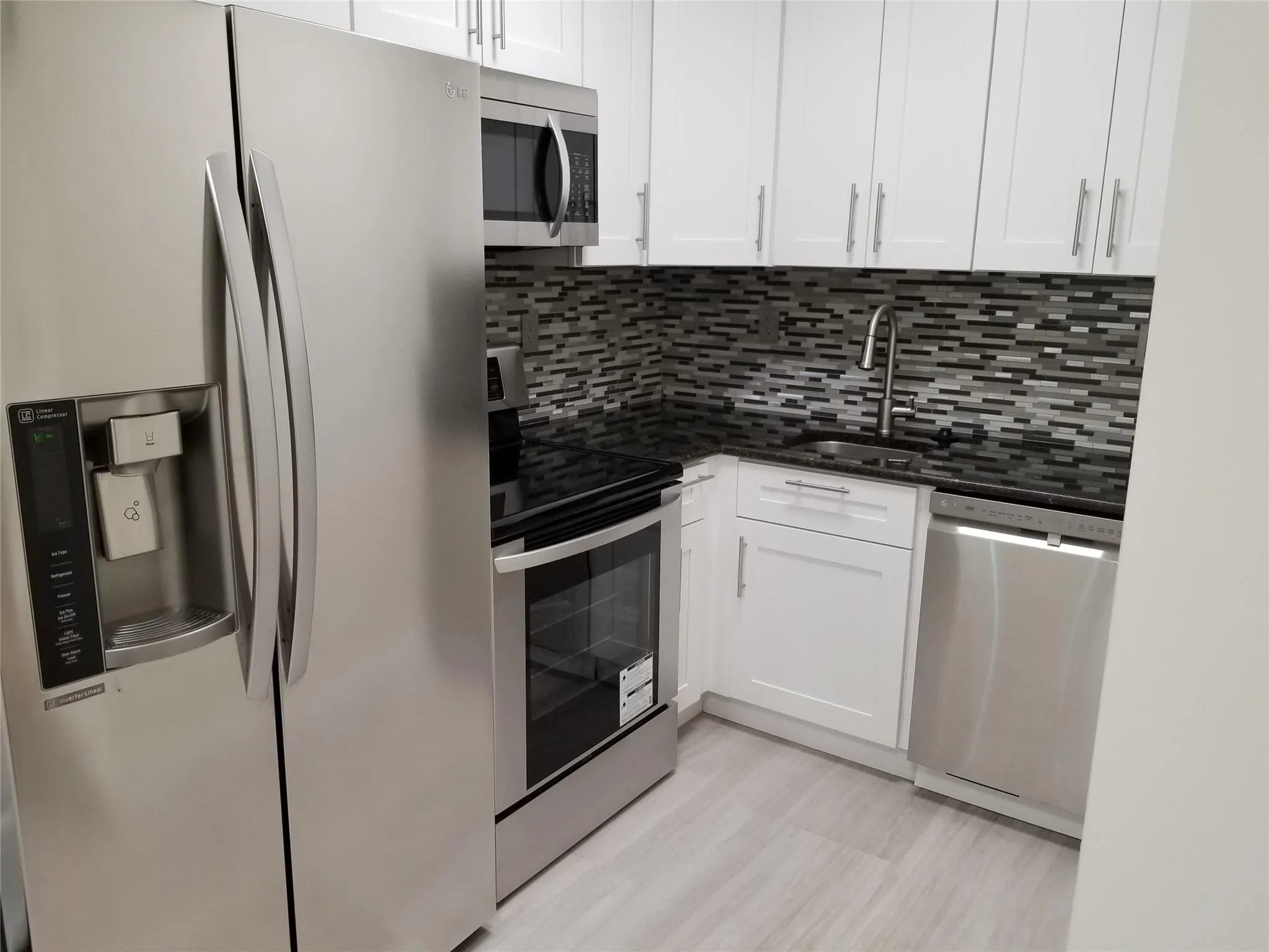 Stainless steel appliances, white cabinetry, dark stone countertops, mosaic tile backsplash, and light-toned flooring