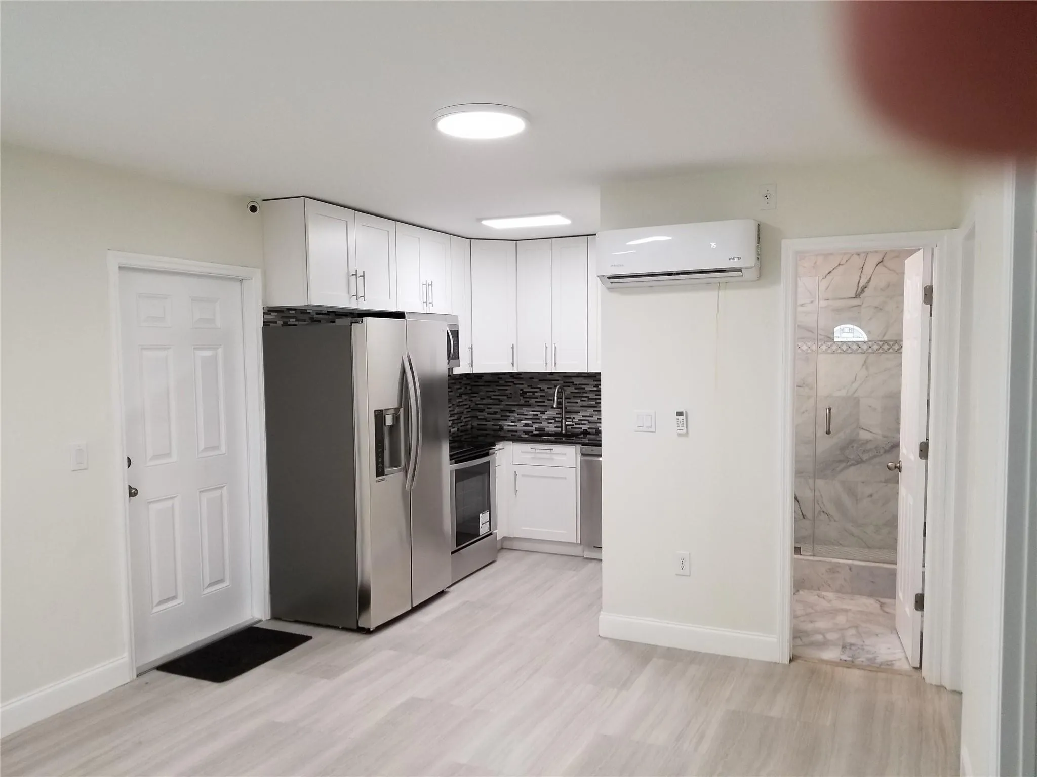 Kitchenette featuring white cabinetry, stainless steel appliances, dark mosaic tile backsplash, and light wood-finish flooring