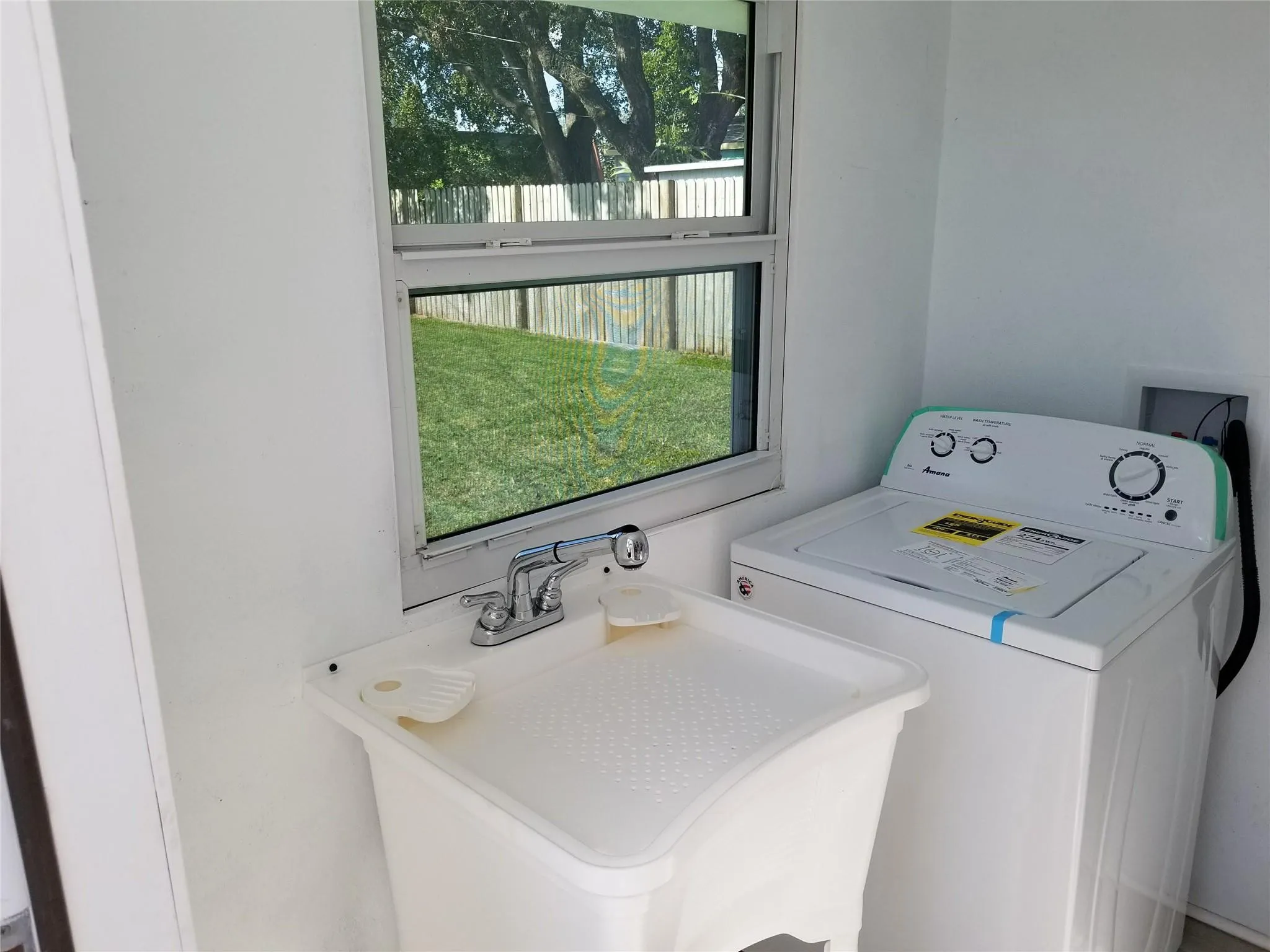 Utility room featuring a window, a laundry sink with a chrome faucet, and white walls