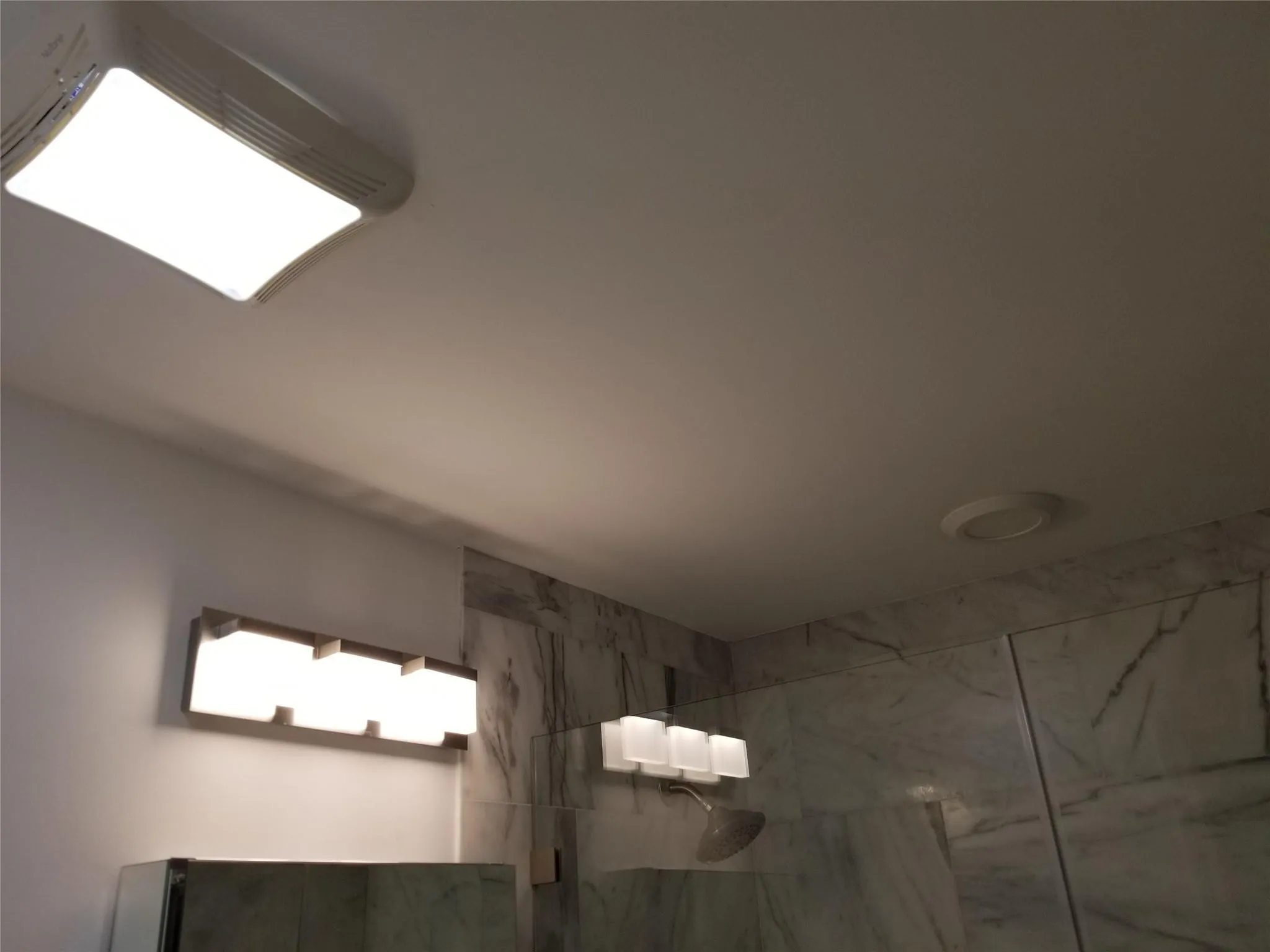 White ceiling with a rectangular flush-mount light fixture, a round recessed light, and wall-mounted vanity lighting