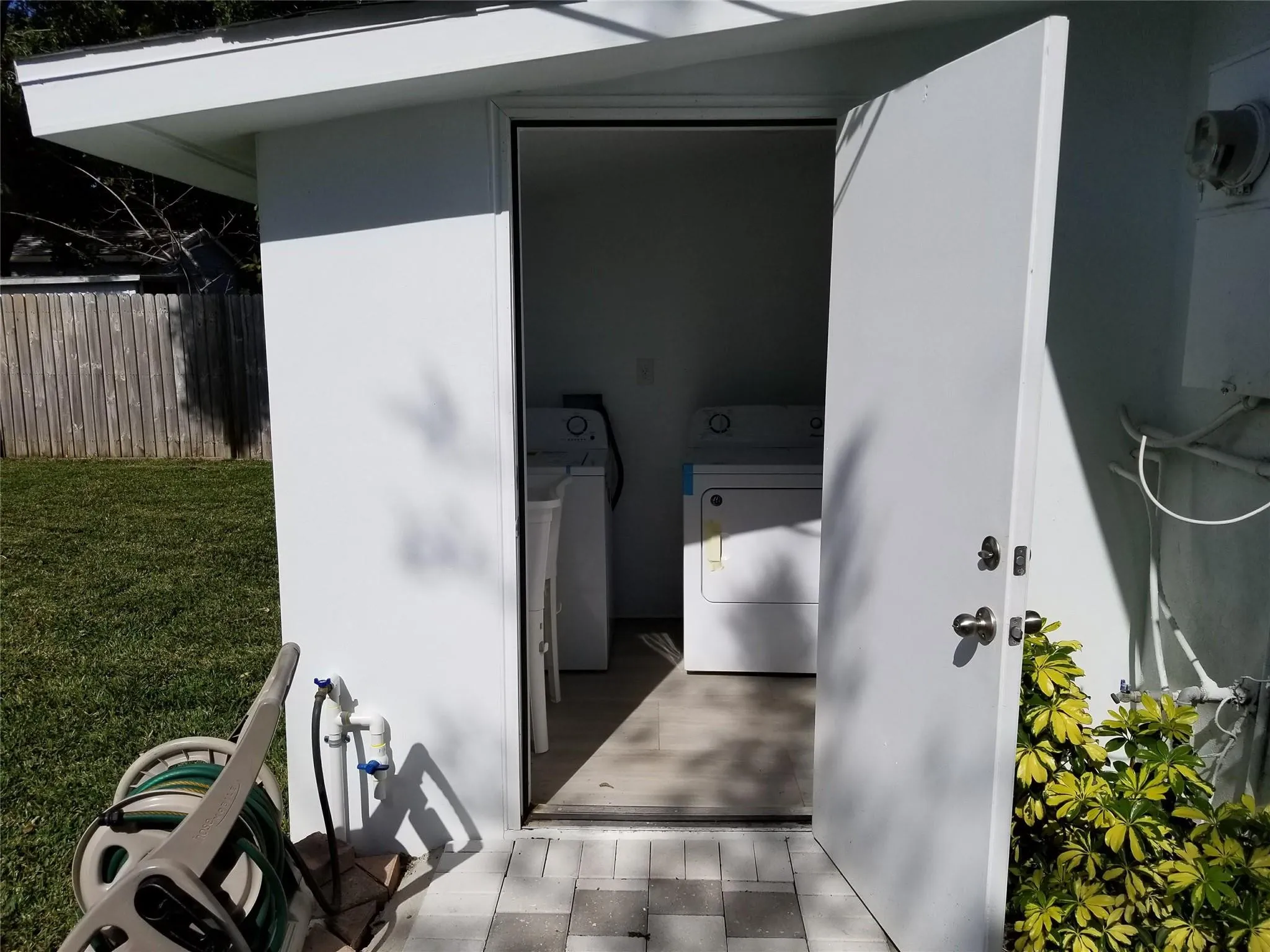 Outdoor utility structure featuring a solid door, paved entry, and a side yard with a wooden fence