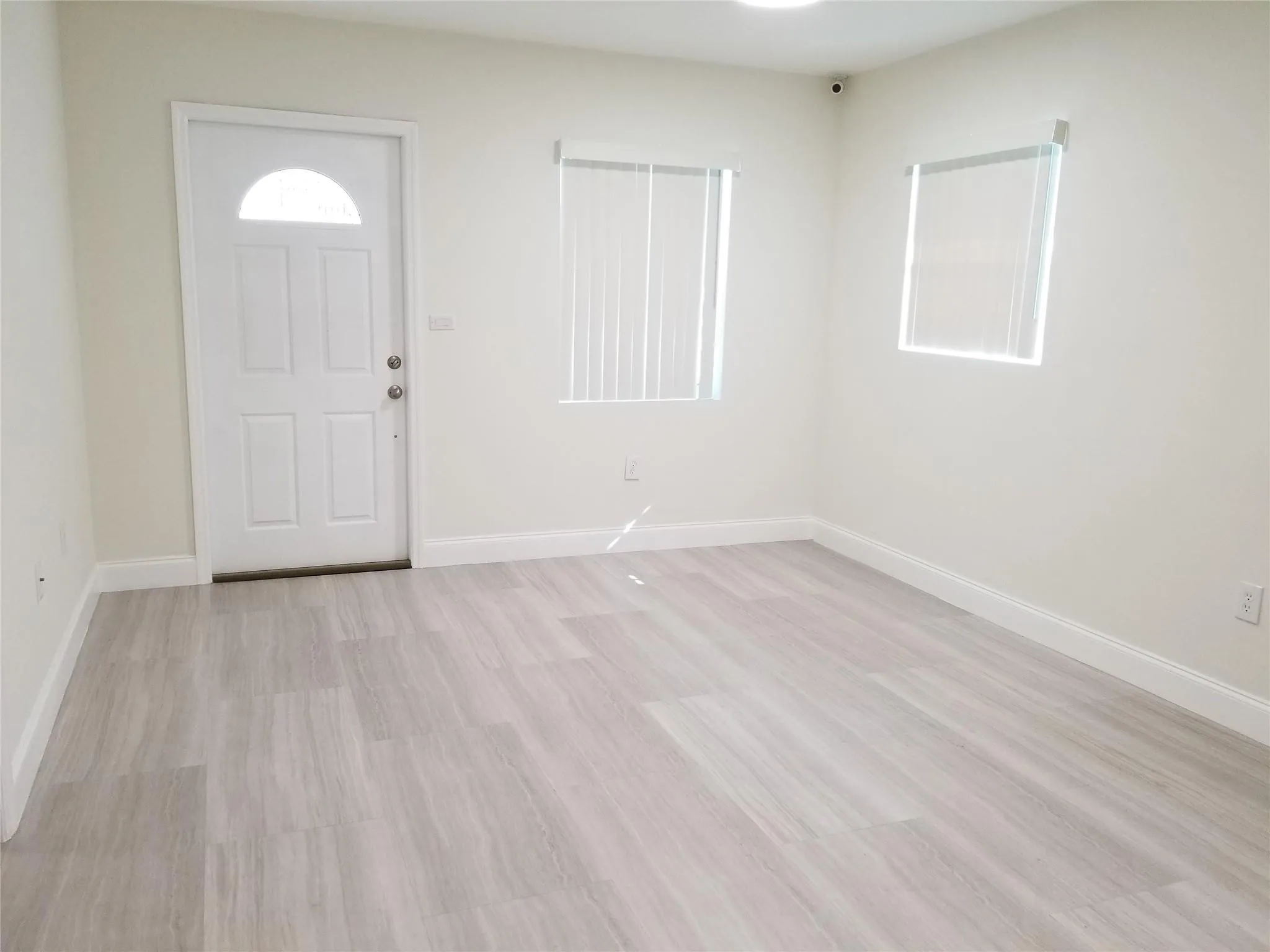 Light-toned wood-finish flooring, white paneled door with an arched lite, multiple windows with blinds, and recessed ceiling lighting