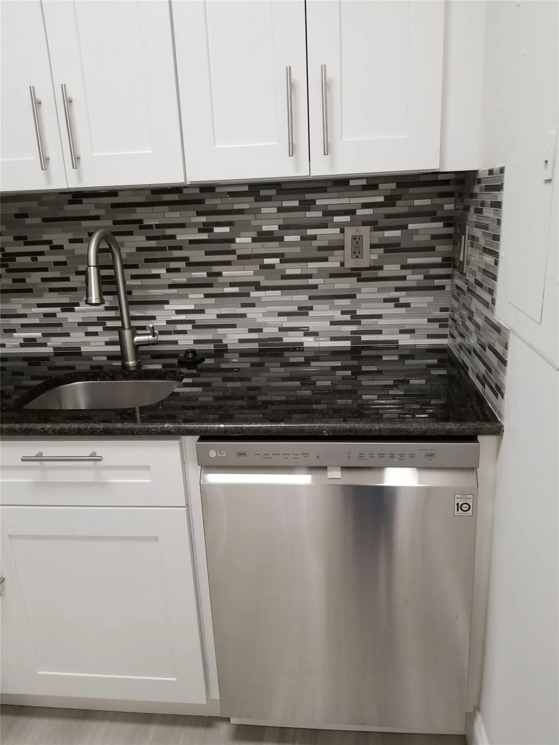 White shaker cabinetry, black granite-style countertop, stainless steel dishwasher, mosaic tile backsplash, and a contemporary gooseneck faucet