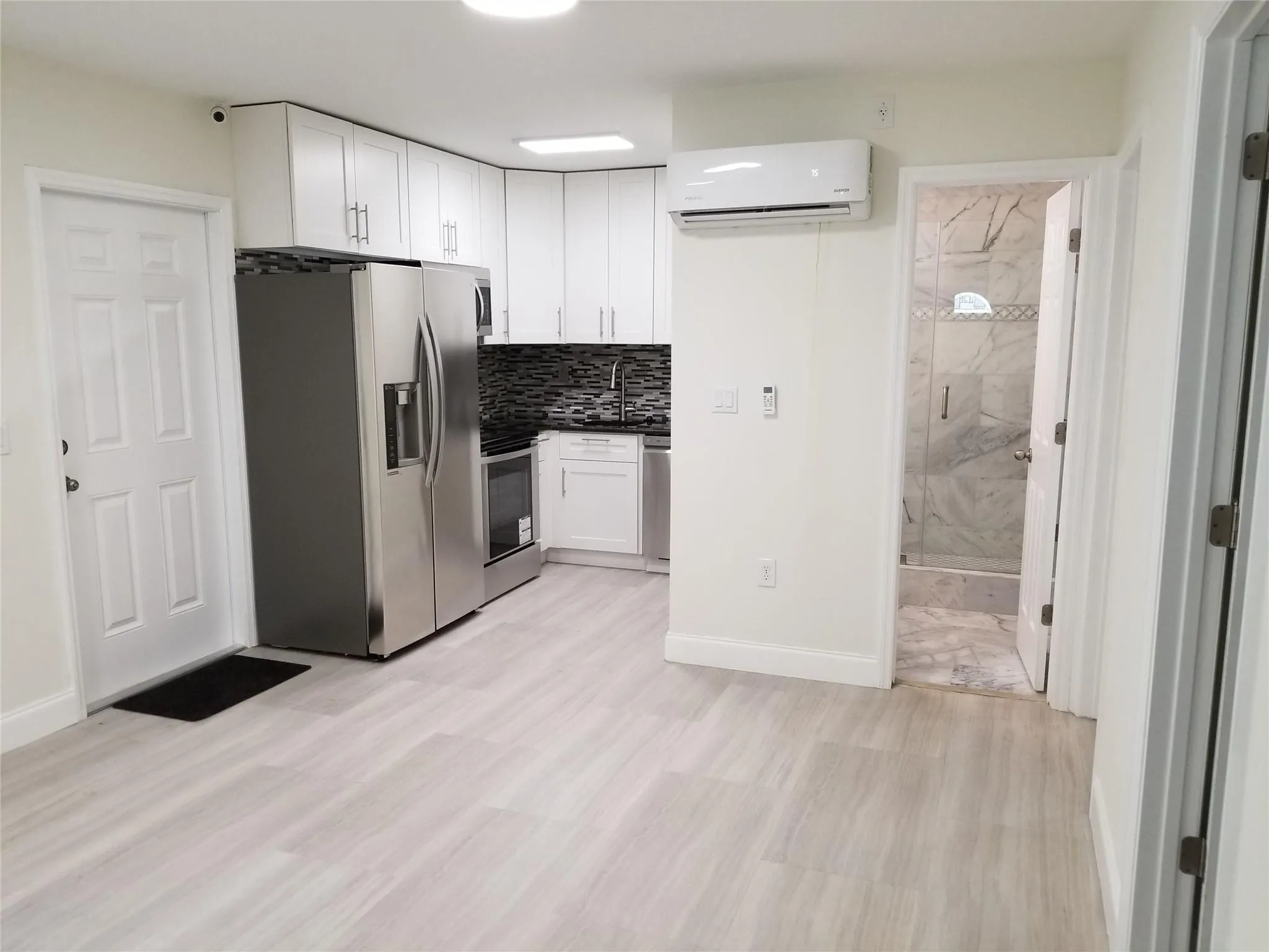 Kitchenette with white cabinetry, stainless steel appliances, and a dark mosaic tile backsplash