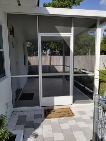 Screened outdoor patio featuring a white frame, wood-finish flooring, and a privacy fence background