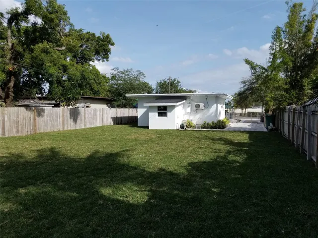 Expansive grassy yard with wood fencing, mature trees, and a paved patio area
