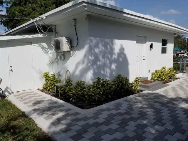 White stucco exterior, two-tone paver pathways, mature landscaping, and an external entry door