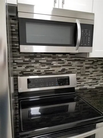 Stainless steel microwave, electric range with a smooth cooktop, mosaic tile backsplash, and dark countertop