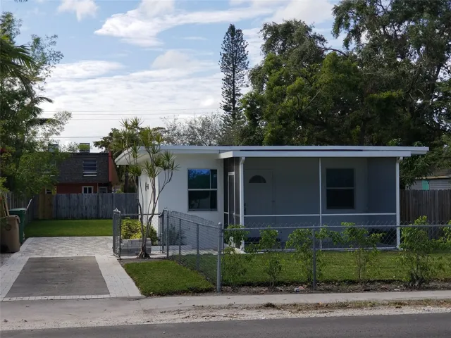 Screened front porch, white exterior, paved driveway, mature landscaping, and chain-link fence