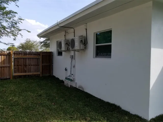 Stucco exterior with multiple wall-mounted HVAC units, featuring a wood fence, grassy area, and a window with a white frame