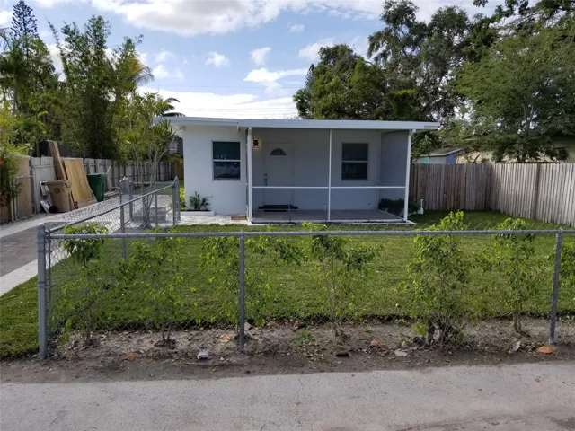 White exterior with a screened front porch, fenced front yard, paved driveway, and mature landscaping