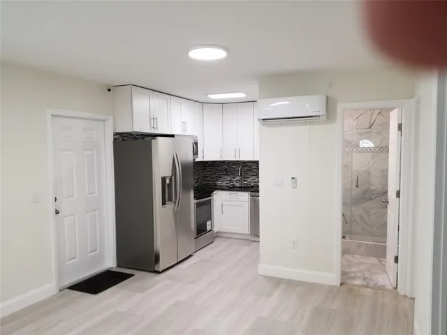 Kitchenette featuring white cabinetry, stainless steel appliances, dark mosaic tile backsplash, and light wood-finish flooring