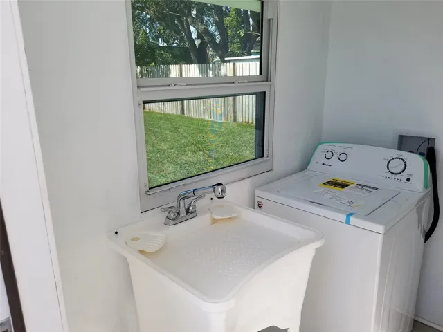 Utility room featuring a window, a laundry sink with a chrome faucet, and white walls