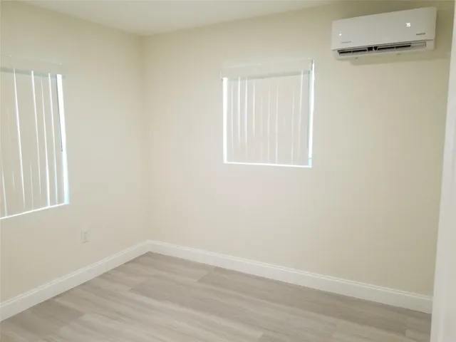Light-toned wood-finish flooring, two windows with vertical blinds, and a wall-mounted air conditioning unit