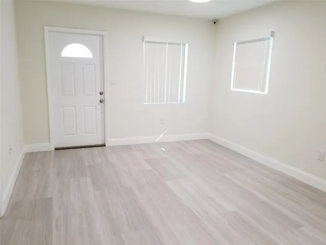 Light-toned wood-finish flooring, white paneled door with an arched lite, multiple windows with blinds, and recessed ceiling lighting