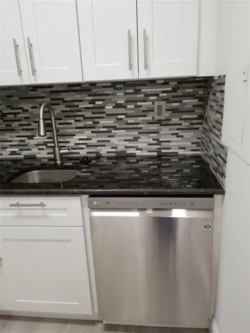 White shaker cabinetry, black granite-style countertop, stainless steel dishwasher, mosaic tile backsplash, and a contemporary gooseneck faucet