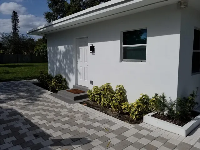 White stucco exterior with a paneled entry door, modern exterior lighting, and a window