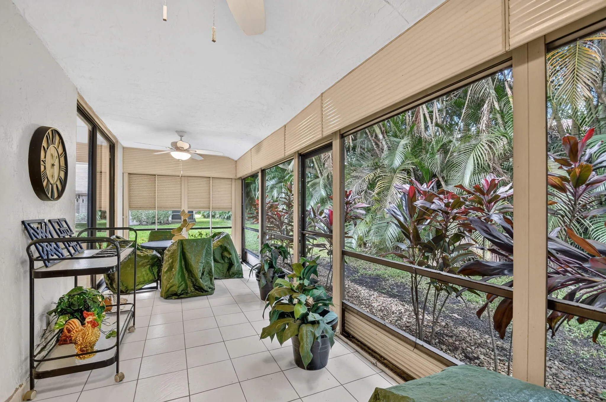 Screened patio featuring white tile flooring, multiple ceiling fans, and expansive window panels