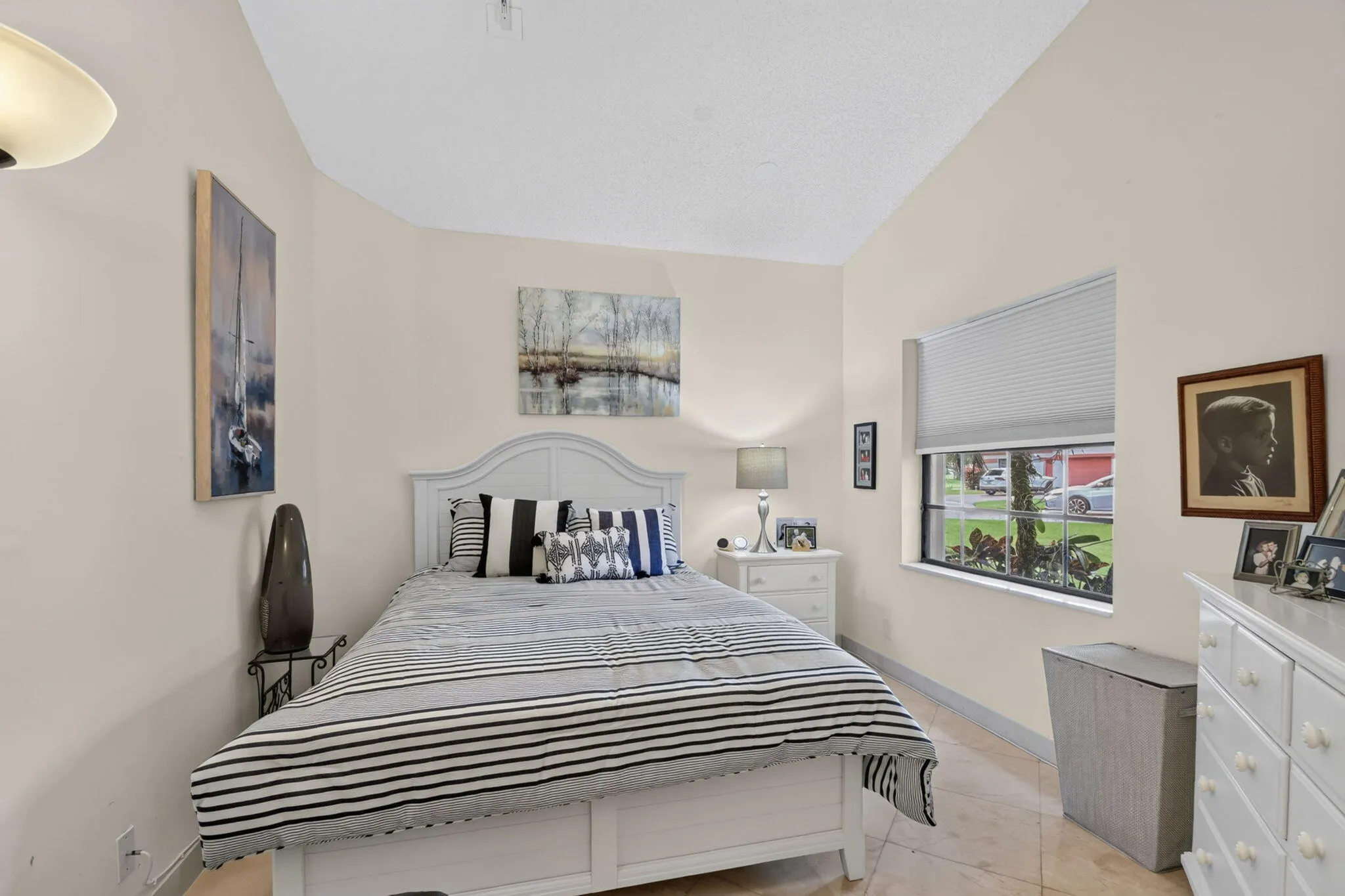Vaulted ceiling, ceiling-mounted light fixture, window with blinds, tile flooring, and light-colored walls