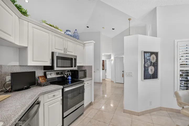 Kitchen featuring white cabinetry, stainless steel appliances, speckled countertops, and a tiled backsplash