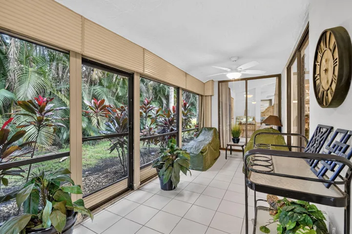 Enclosed sunroom featuring white tile flooring, ceiling fan, and large windows with horizontal blinds