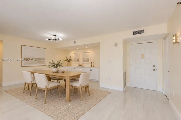 Neutral-toned interior space featuring polished tile flooring, recessed cove lighting, built-in cabinetry, a multi-arm modern light fixture, and a six-panel entry door