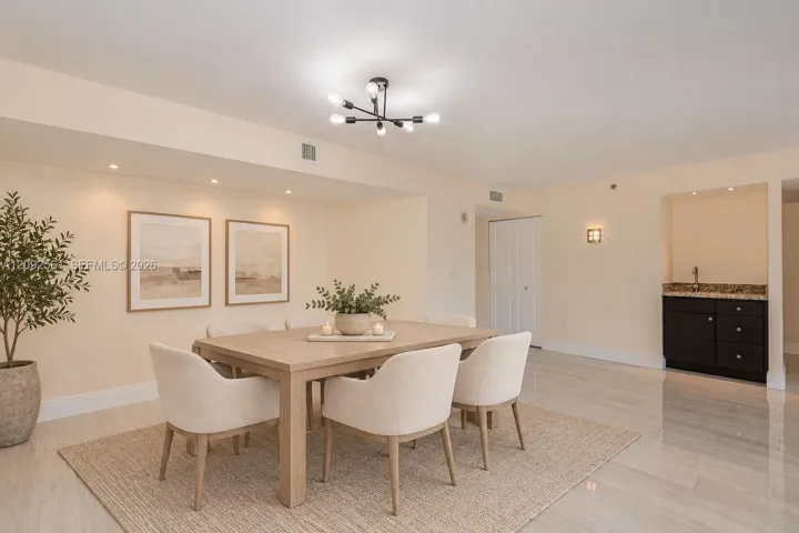 Dining area featuring stone-finish flooring, a multi-arm modern chandelier, recessed lighting, and a built-in wet bar with dark cabinetry and a stone countertop