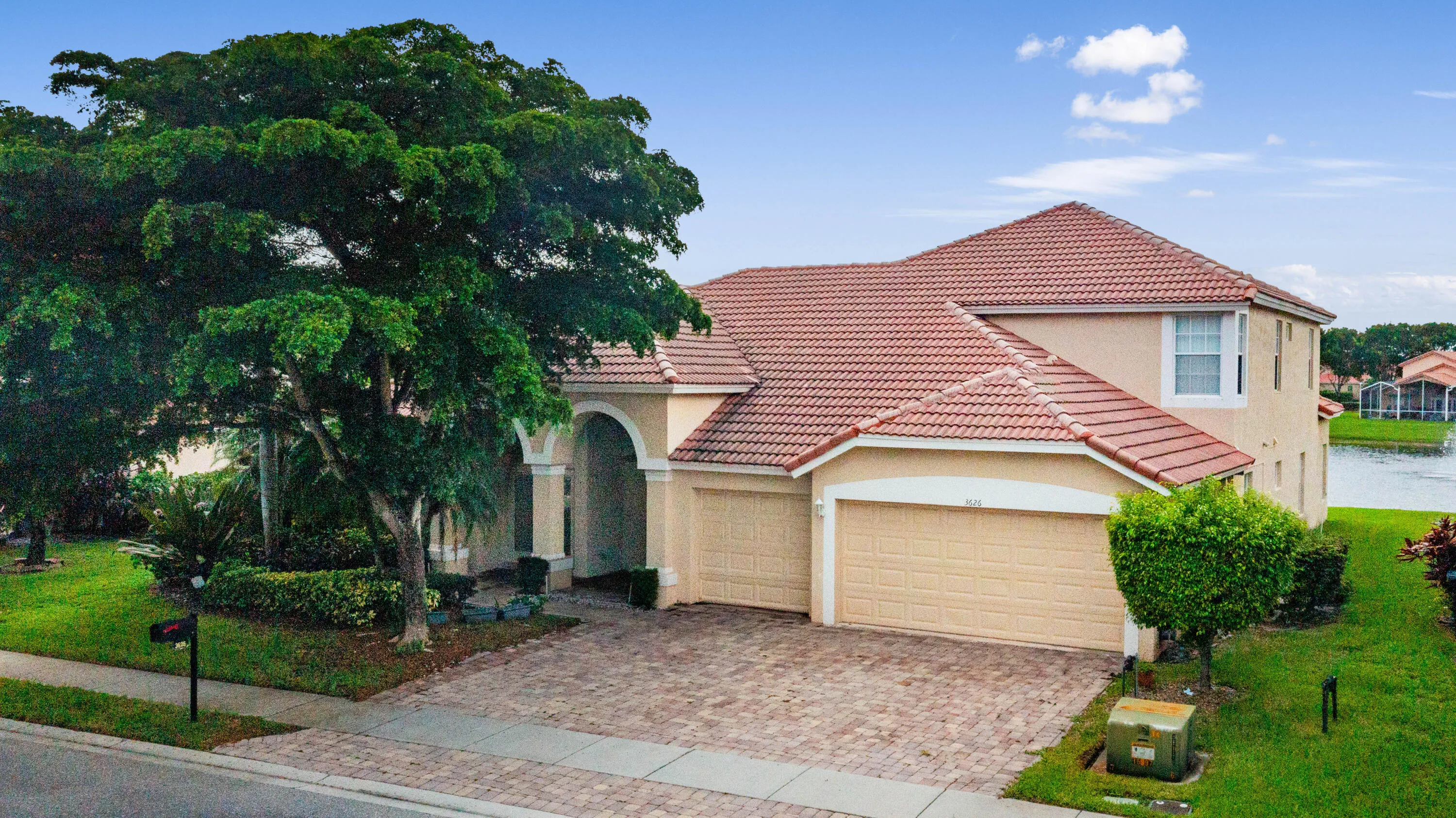 Two-story stucco exterior with a tiled roof, arched entryway, and a paver driveway