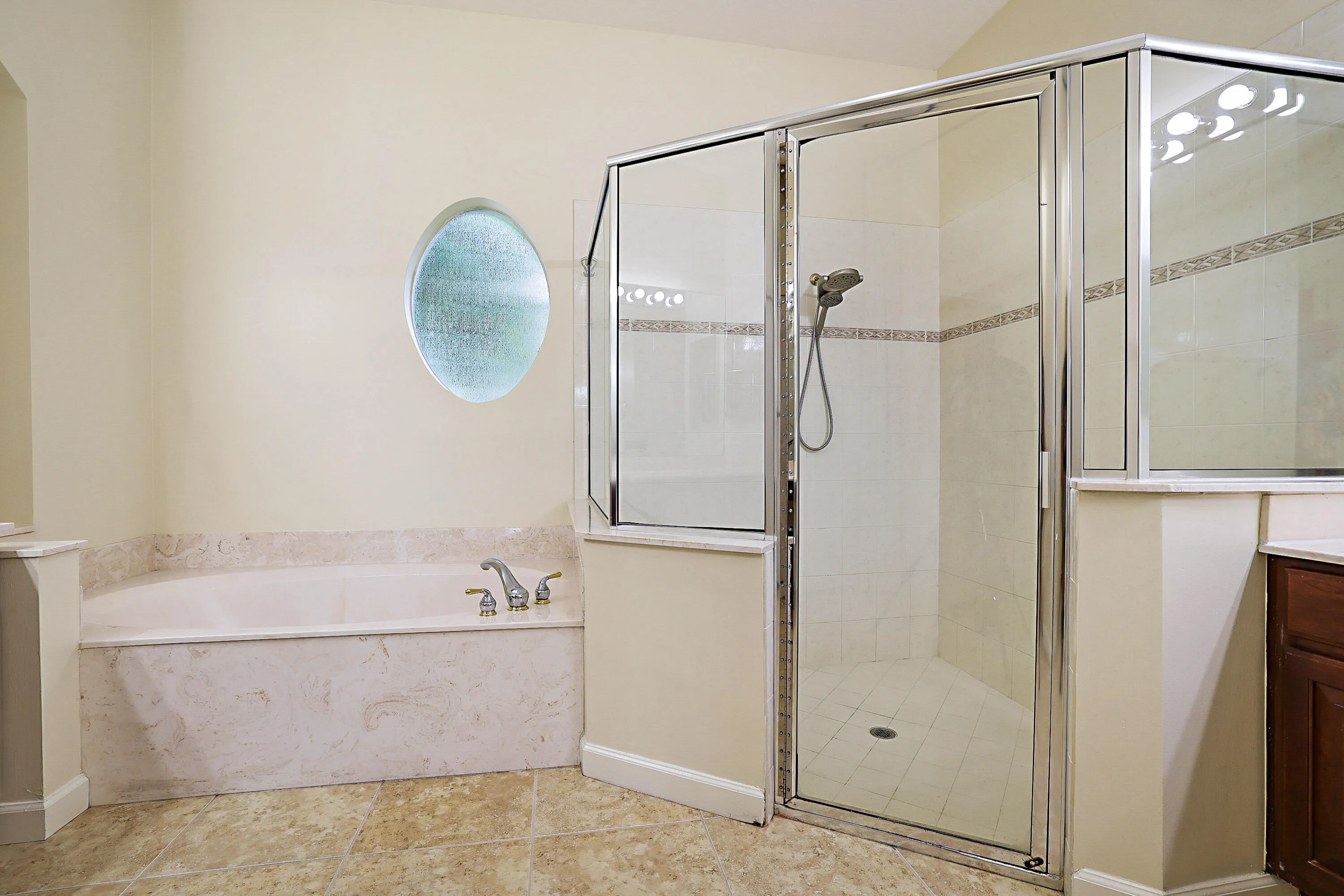 Recessed soaking tub with stone surround, circular privacy window, glass-enclosed shower with tile surround, and tile flooring