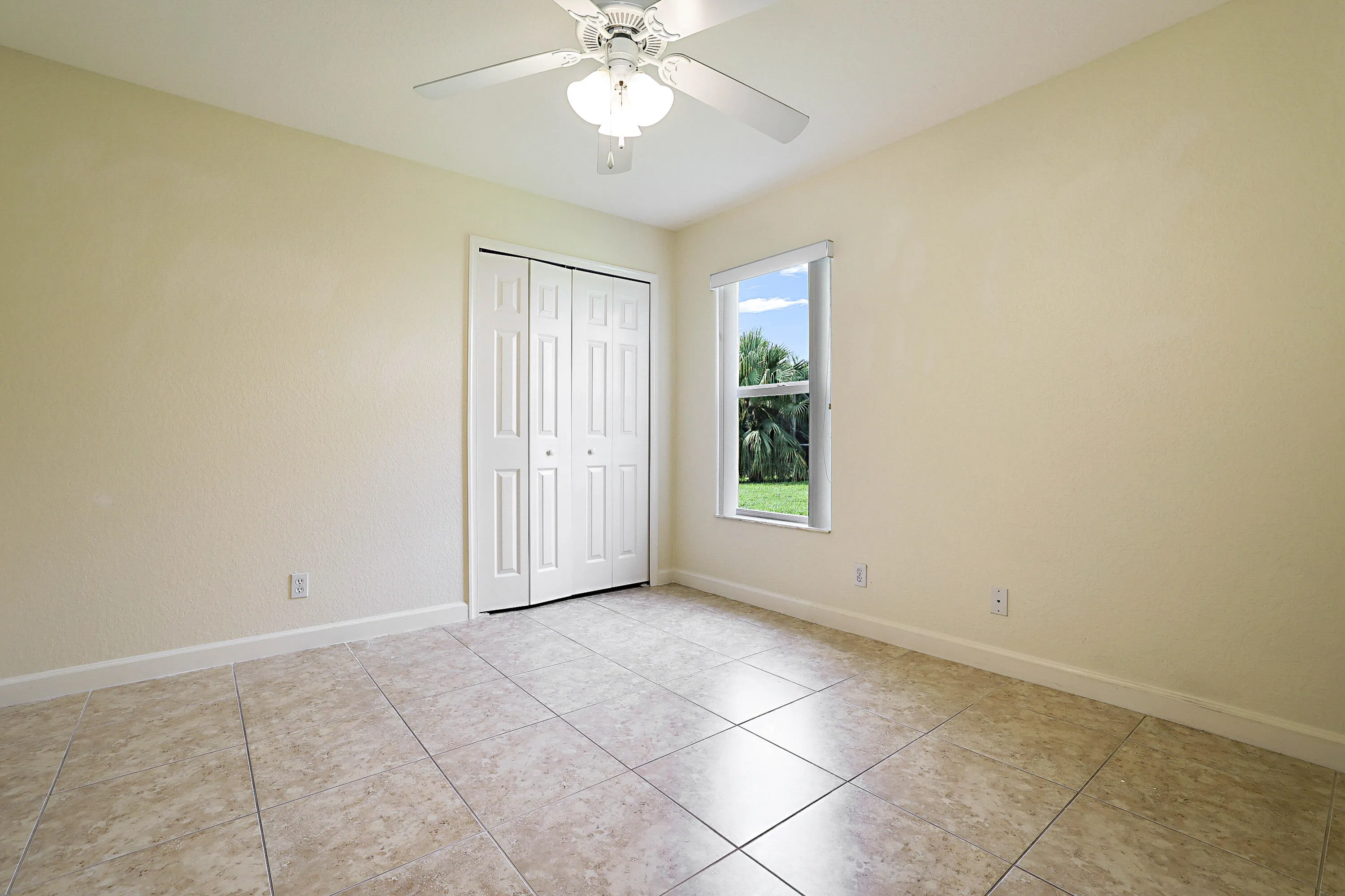 Neutral-toned ceramic tile flooring, bi-fold closet doors, and a ceiling fan with integrated lighting