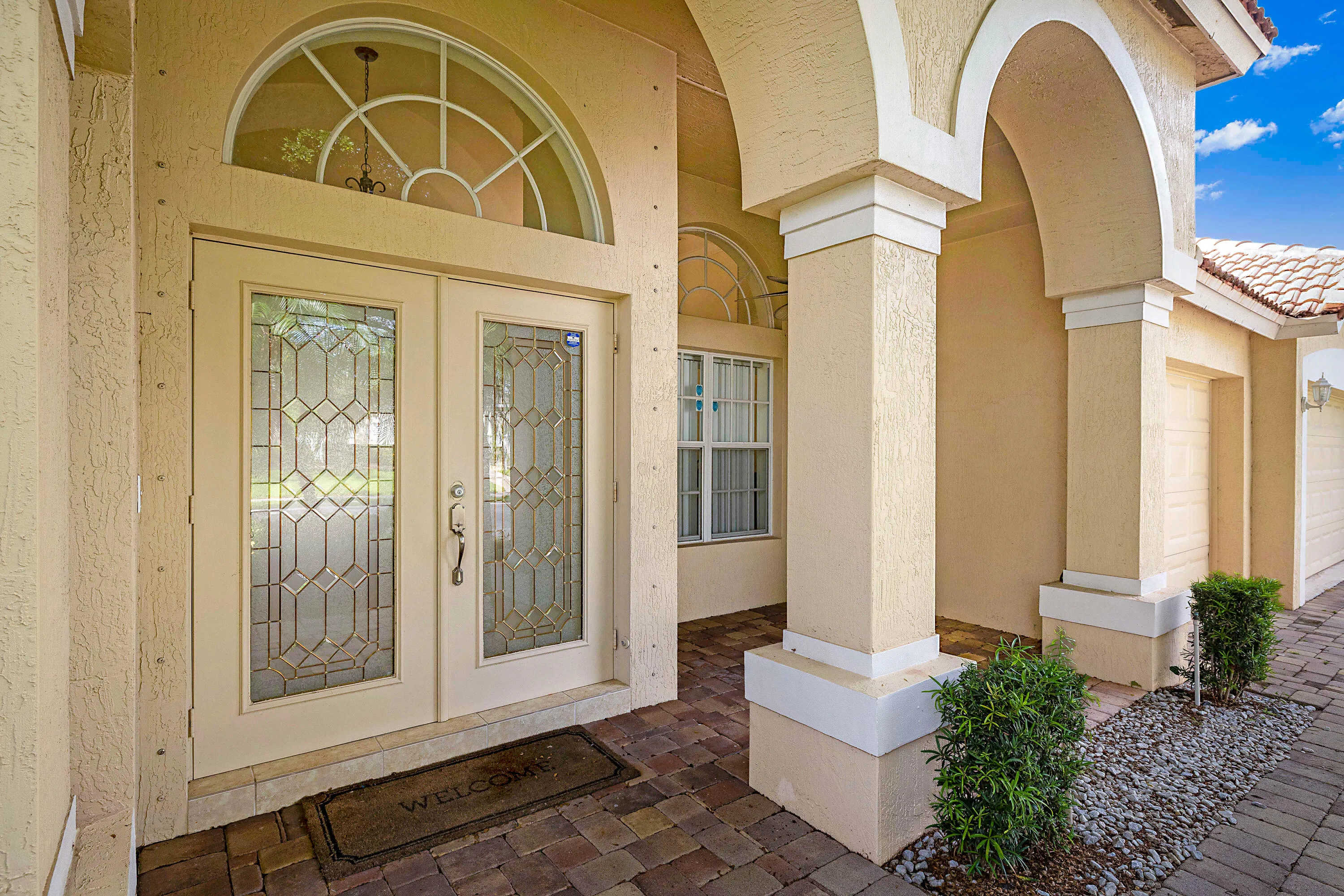 Elegant covered entry featuring a grand transom-topped glass and wood door, decorative leaded-glass sidelights, and soaring barrel-vault archways supported by substantial columns
