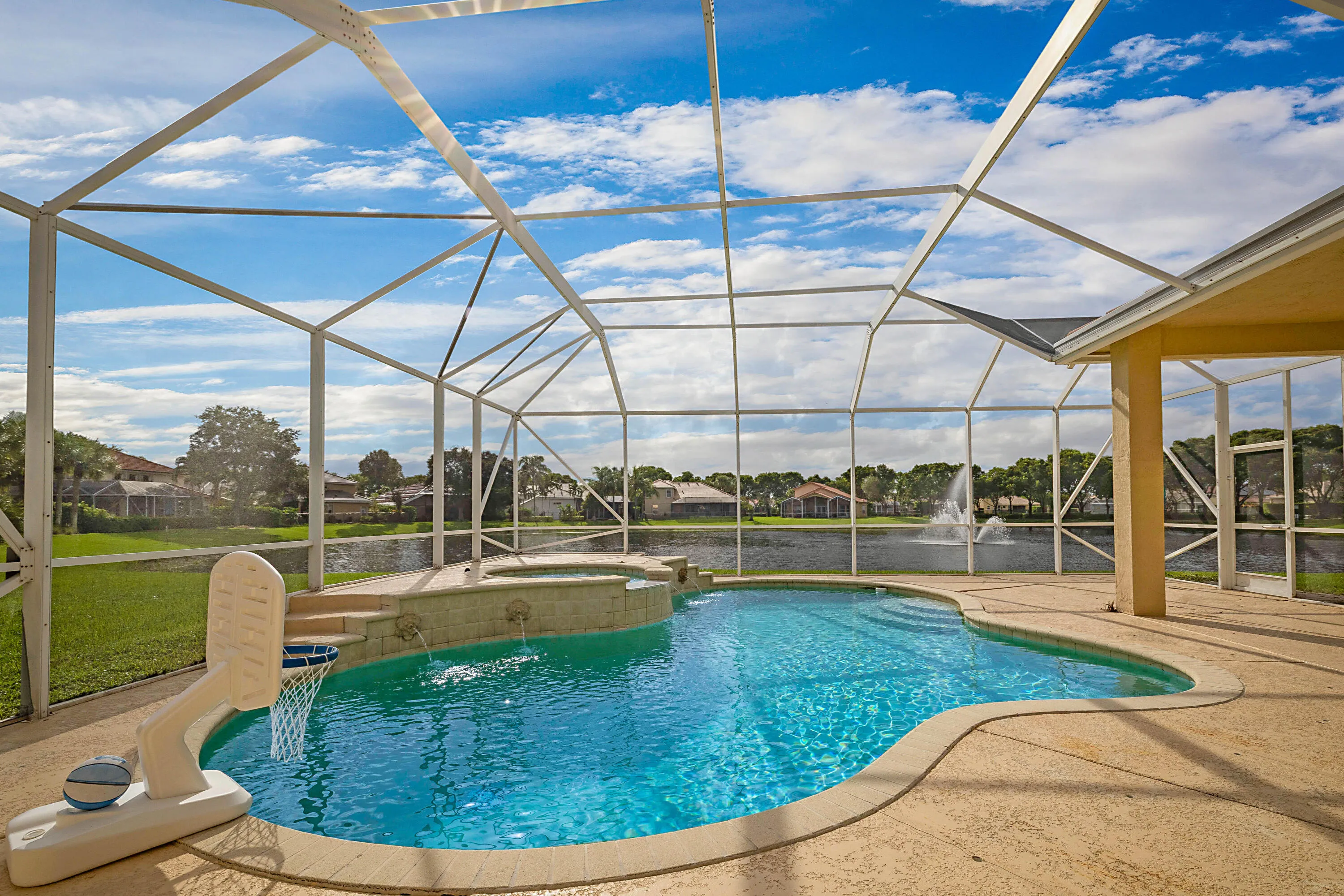 Screened-in outdoor pool and spa with integrated steps, surrounded by a concrete patio and a serene pond backdrop