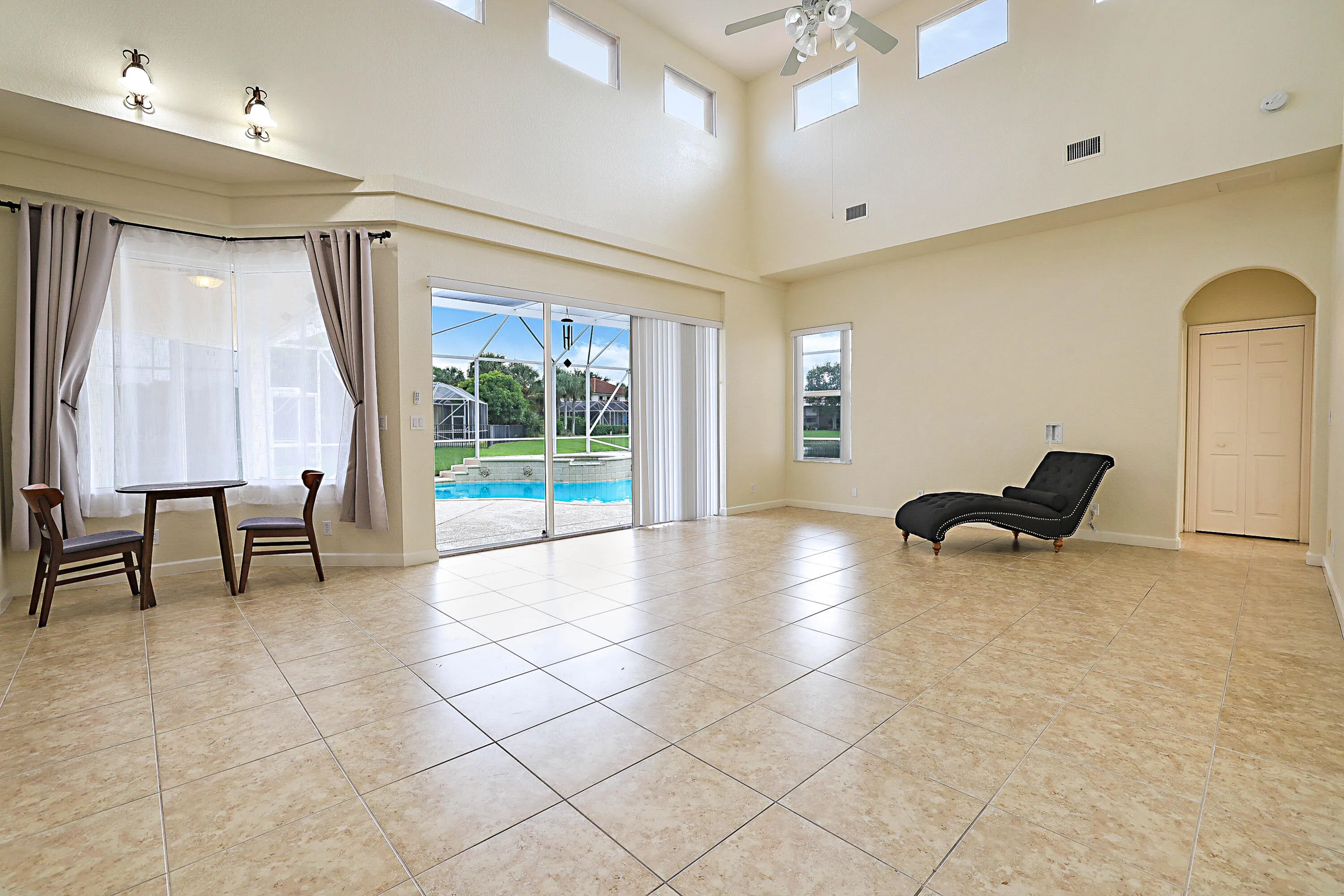 Vaulted ceiling with transom windows, tile flooring, sliding glass doors to pool, and an arched entry